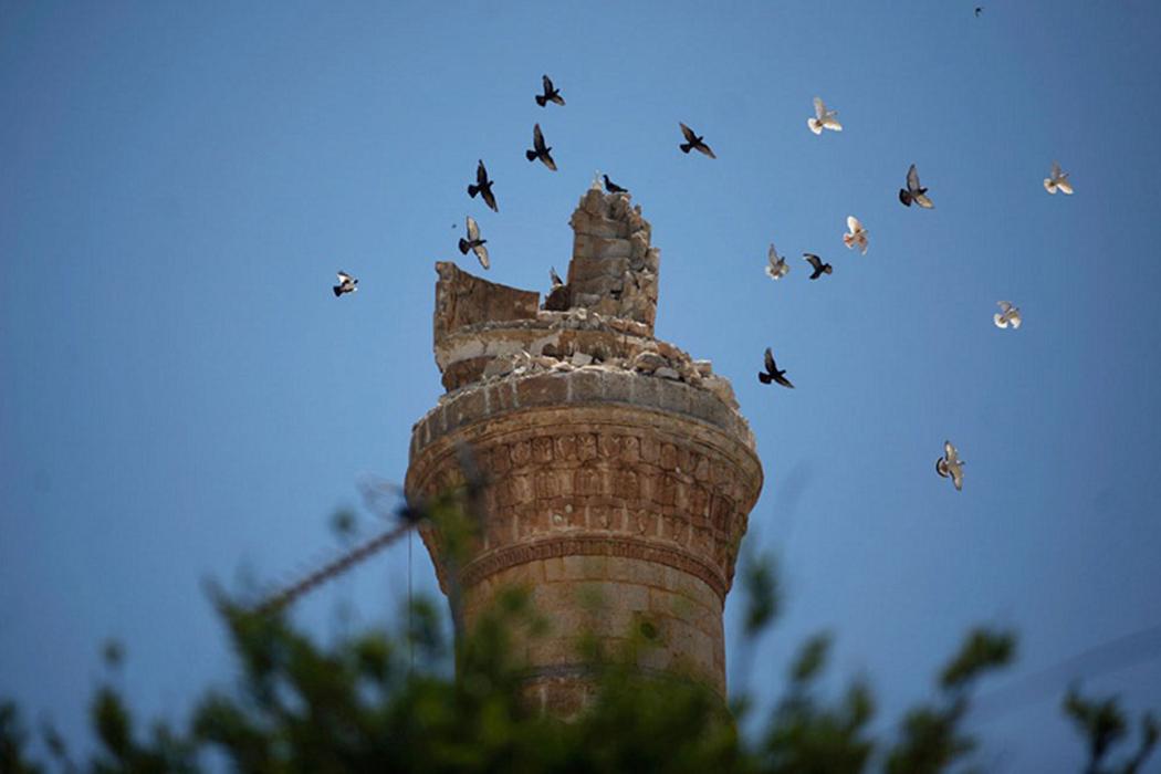 Птицы пролетают над разрушенным минаретом мечети в северном городе Ариха